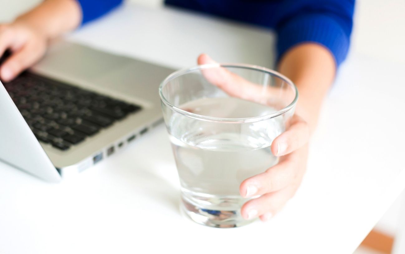 A glass of water next to a laptop.