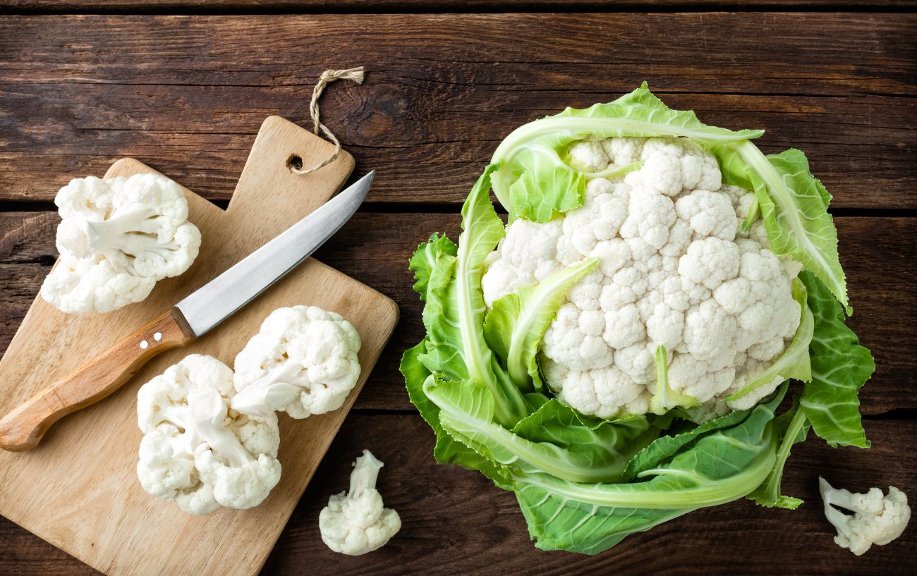 A head of cauliflower is cut on a cutting board.