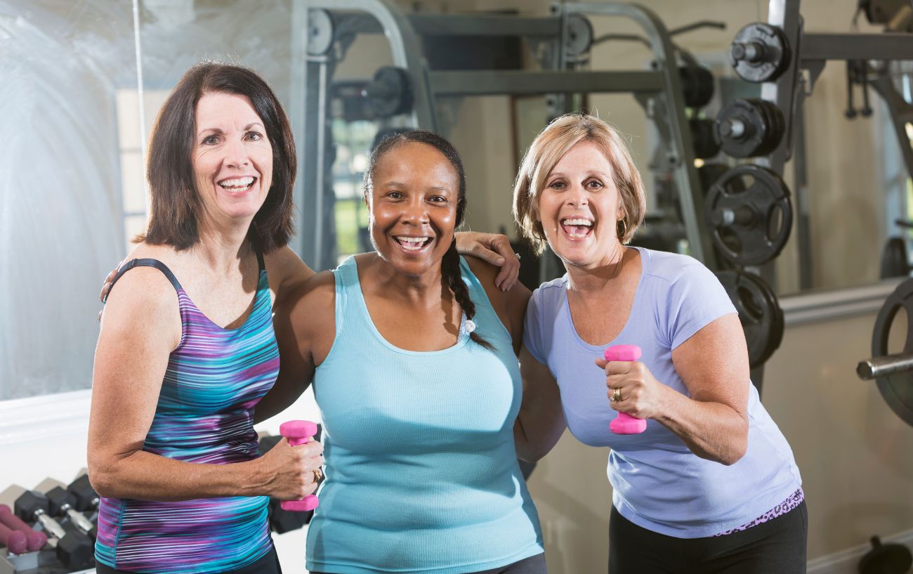 Three women over 50 holding dumbbells at the gym.