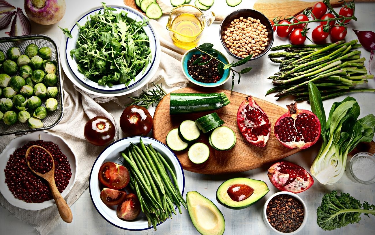 A wide variety of food spread on a table, such as vegetables, leafy greens, fruits, and oil.